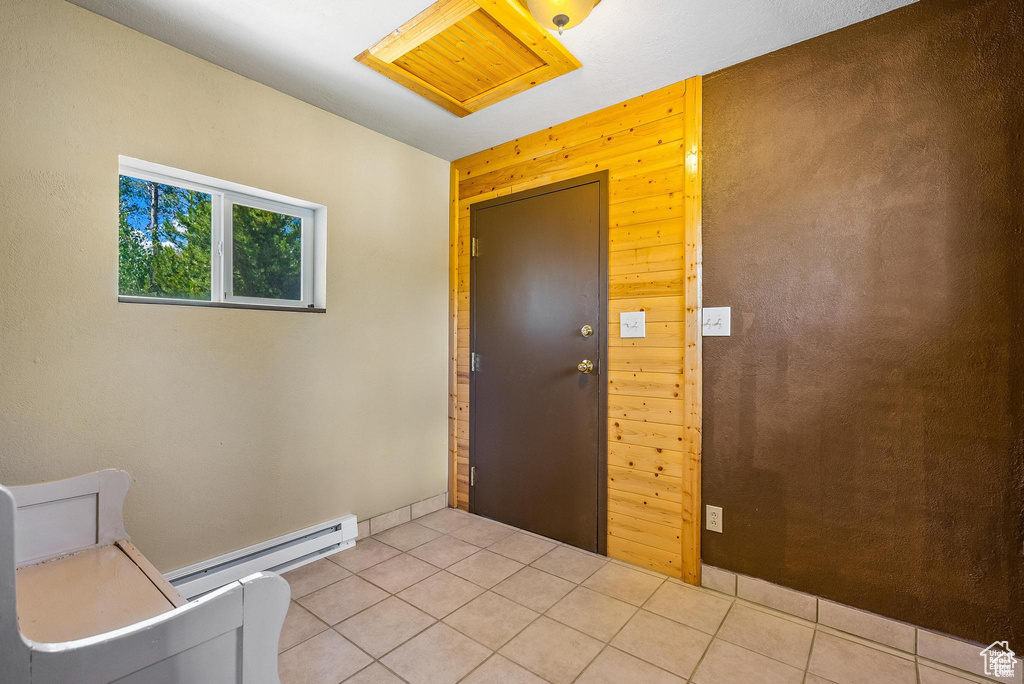 Entryway with a baseboard radiator, light tile patterned flooring, and wood walls