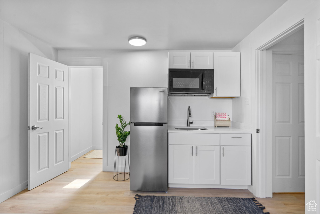 Kitchen with freestanding refrigerator, black microwave, a sink, light wood-style floors, and white cabinets