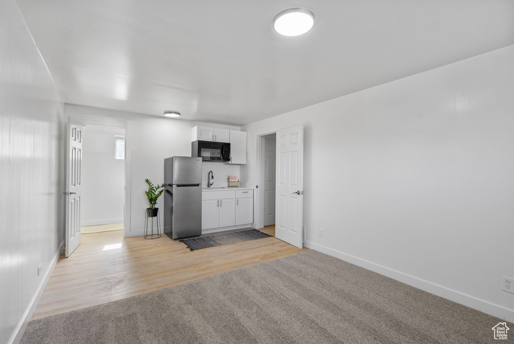 Kitchen with freestanding refrigerator, black microwave, a sink, baseboards, and white cabinets