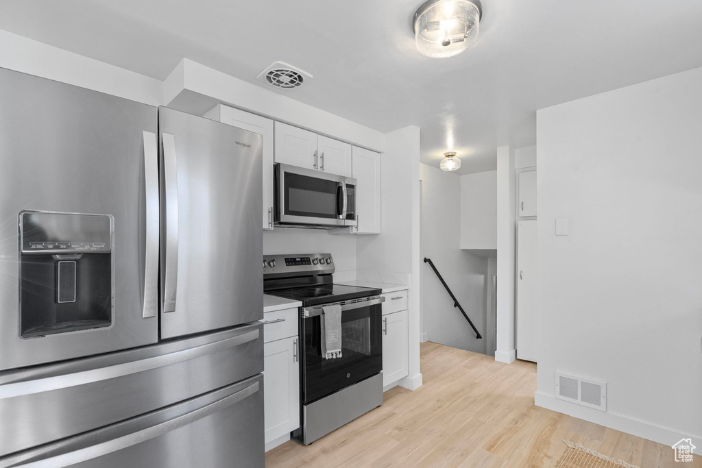 Kitchen with appliances with stainless steel finishes, white cabinetry, light countertops, and light wood-type flooring