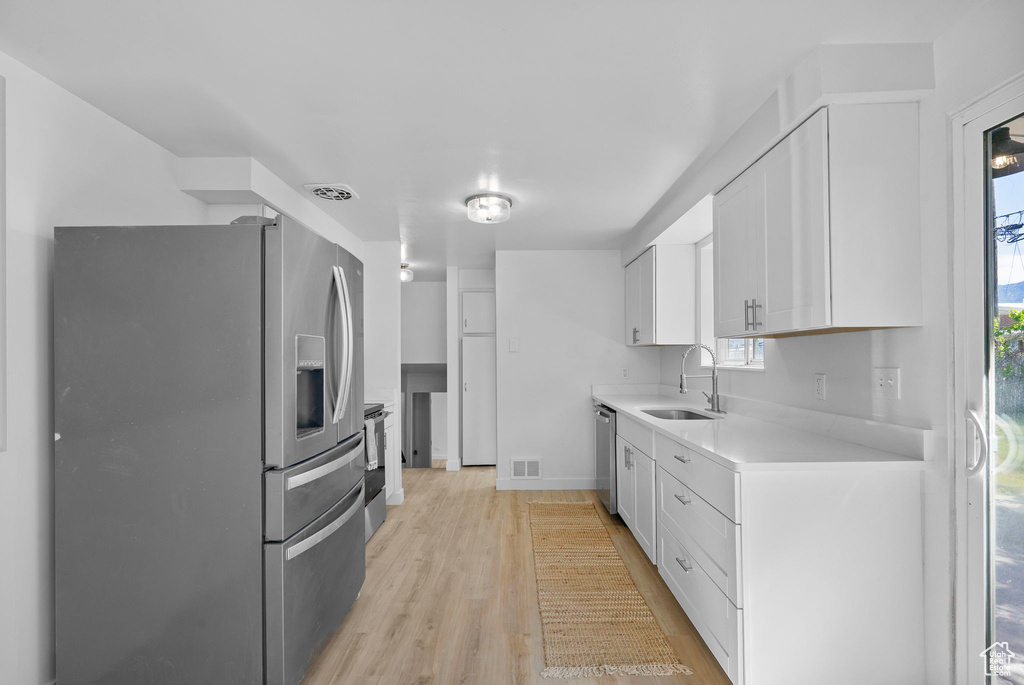 Kitchen featuring appliances with stainless steel finishes, a sink, light countertops, white cabinetry, and light wood-style flooring