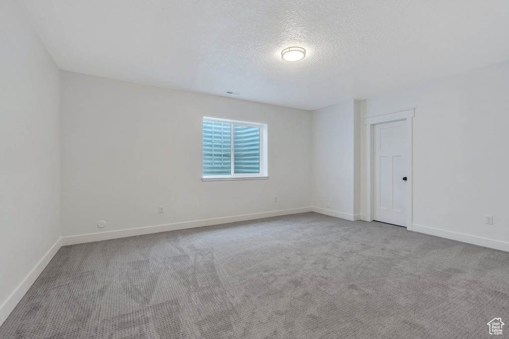Carpeted spare room with a textured ceiling and baseboards