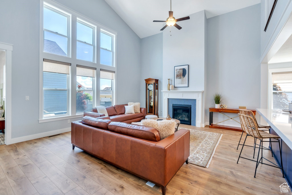 Living area with high vaulted ceiling, light wood-style flooring, a glass covered fireplace, a ceiling fan, and baseboards