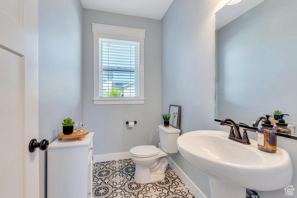 Half bathroom featuring toilet, baseboards, tile patterned flooring, and a sink