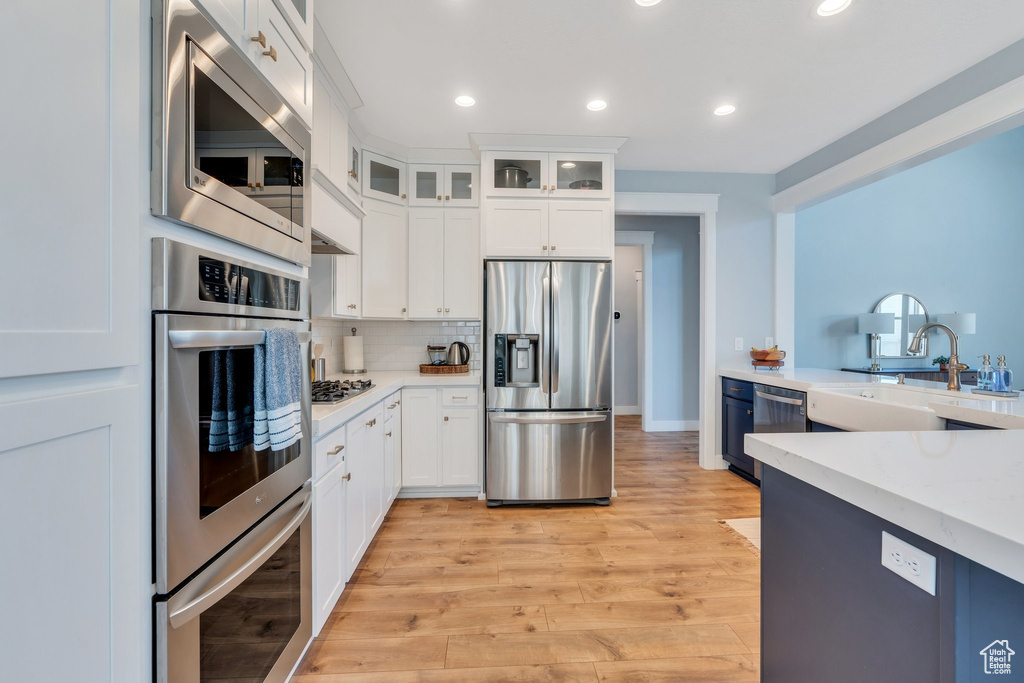 Kitchen featuring stainless steel appliances, a sink, white cabinetry, glass insert cabinets, and light wood-type flooring