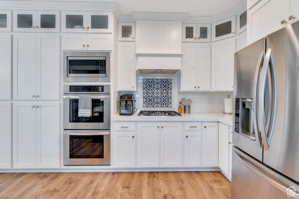 Kitchen with stainless steel appliances, light countertops, white cabinetry, and light wood-style floors
