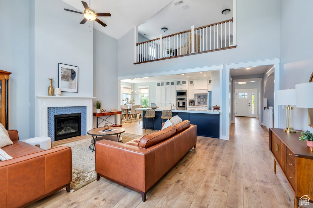 Living room featuring high vaulted ceiling, healthy amount of natural light, a ceiling fan, light wood-type flooring, and a glass covered fireplace