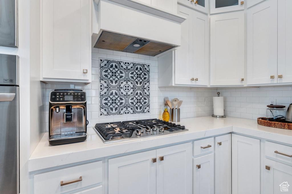 Kitchen featuring custom exhaust hood, stainless steel gas cooktop, oven, and backsplash