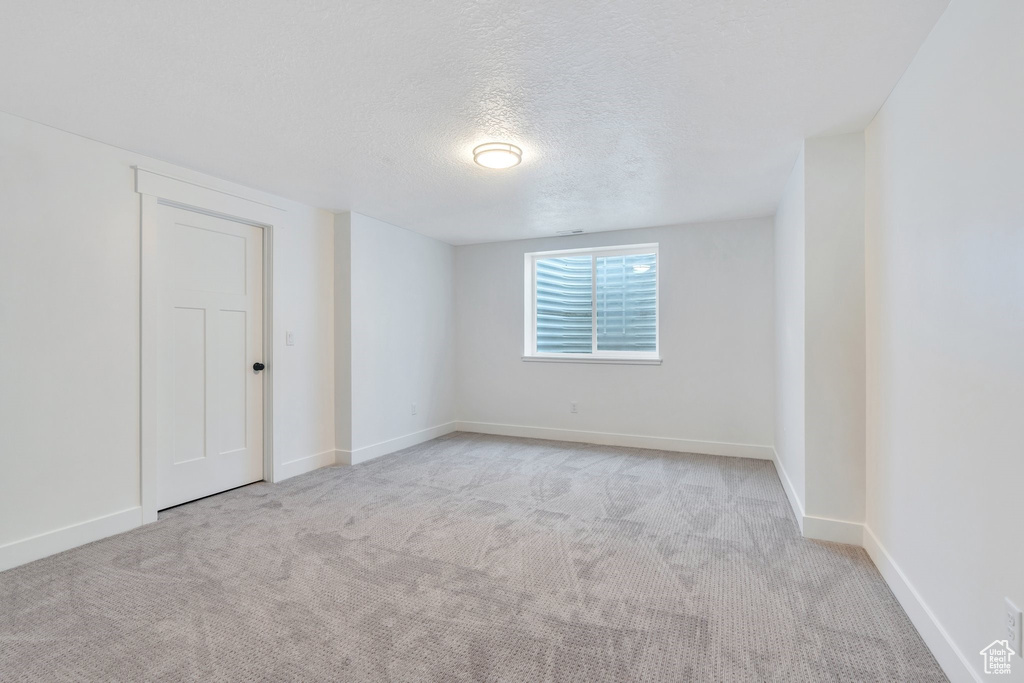 Empty room featuring light colored carpet, a textured ceiling, and baseboards