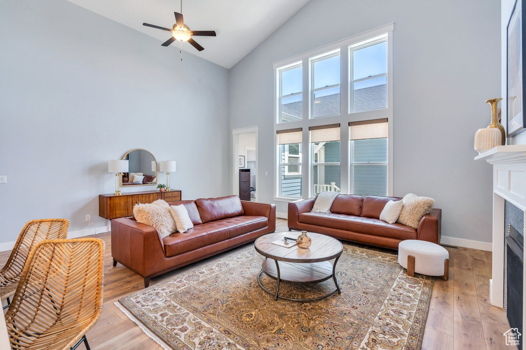 Living area featuring high vaulted ceiling, ceiling fan, a fireplace, light wood-type flooring, and baseboards