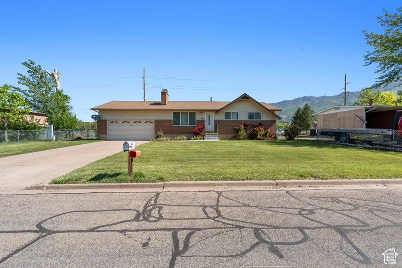 Ranch-style house featuring driveway, an attached garage, a chimney, a mountain view, and brick siding