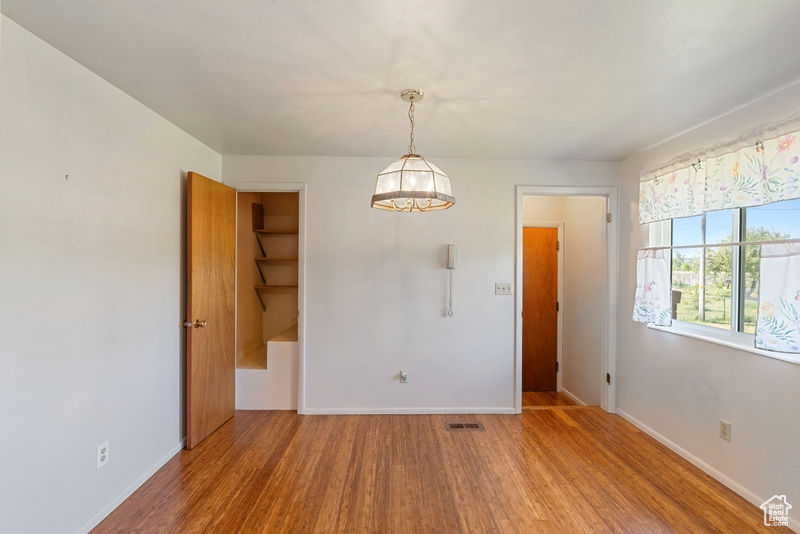 Unfurnished dining area featuring baseboards, wood finished floors, and a chandelier
