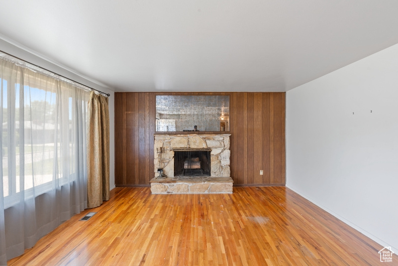 Unfurnished living room featuring a stone fireplace, wood finished floors, wood walls, and baseboards