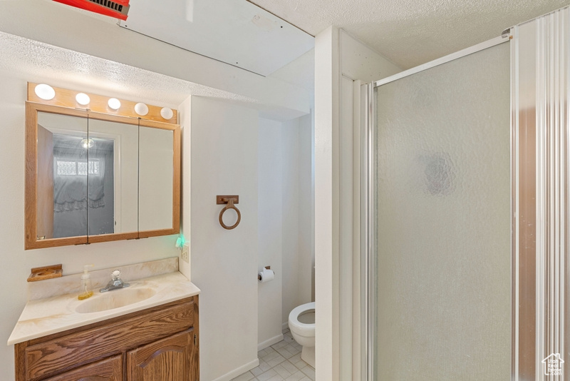 Full bathroom with a shower stall, vanity, toilet, tile patterned floors, and a textured ceiling