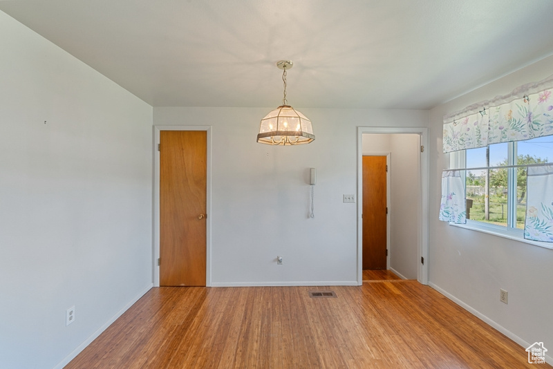 Unfurnished dining area with wood finished floors, baseboards, and a chandelier