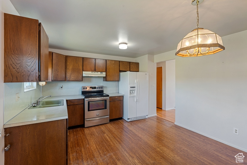 Kitchen featuring stainless steel electric stove, white refrigerator with ice dispenser, a sink, light countertops, and under cabinet range hood