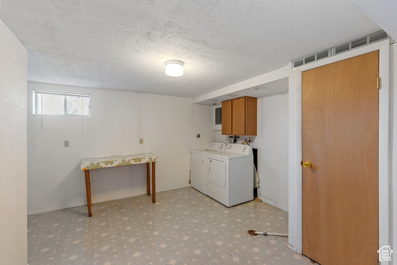 Laundry area with cabinet space, washing machine and dryer, light floors, and a textured ceiling