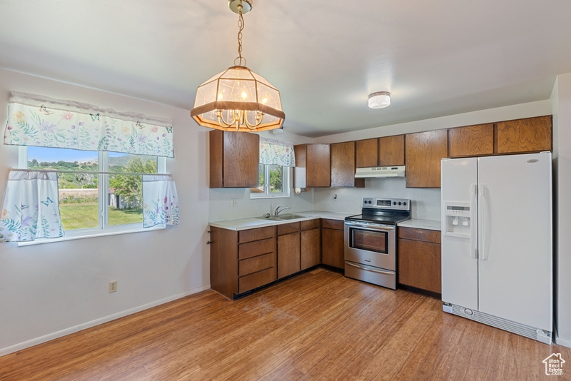Kitchen with white refrigerator with ice dispenser, electric stove, under cabinet range hood, light countertops, and brown cabinets