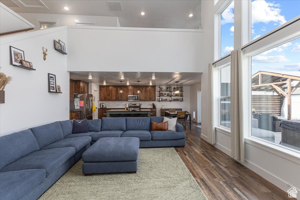 Living room featuring a towering ceiling, dark wood-style floors, healthy amount of natural light, recessed lighting, and baseboards