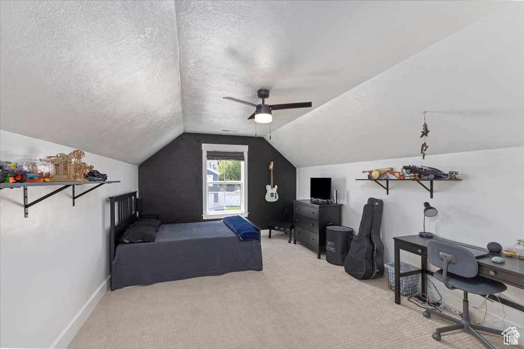 Carpeted bedroom featuring vaulted ceiling, a textured ceiling, a desk, ceiling fan, and baseboards