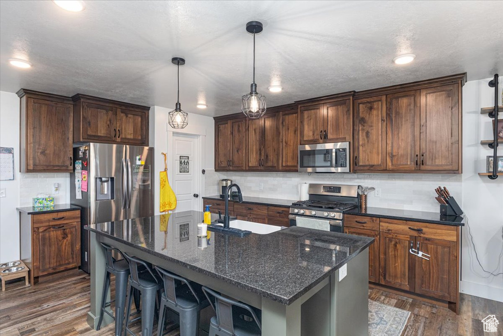 Kitchen featuring stainless steel appliances, a sink, tasteful backsplash, dark wood-type flooring, and dark stone counters