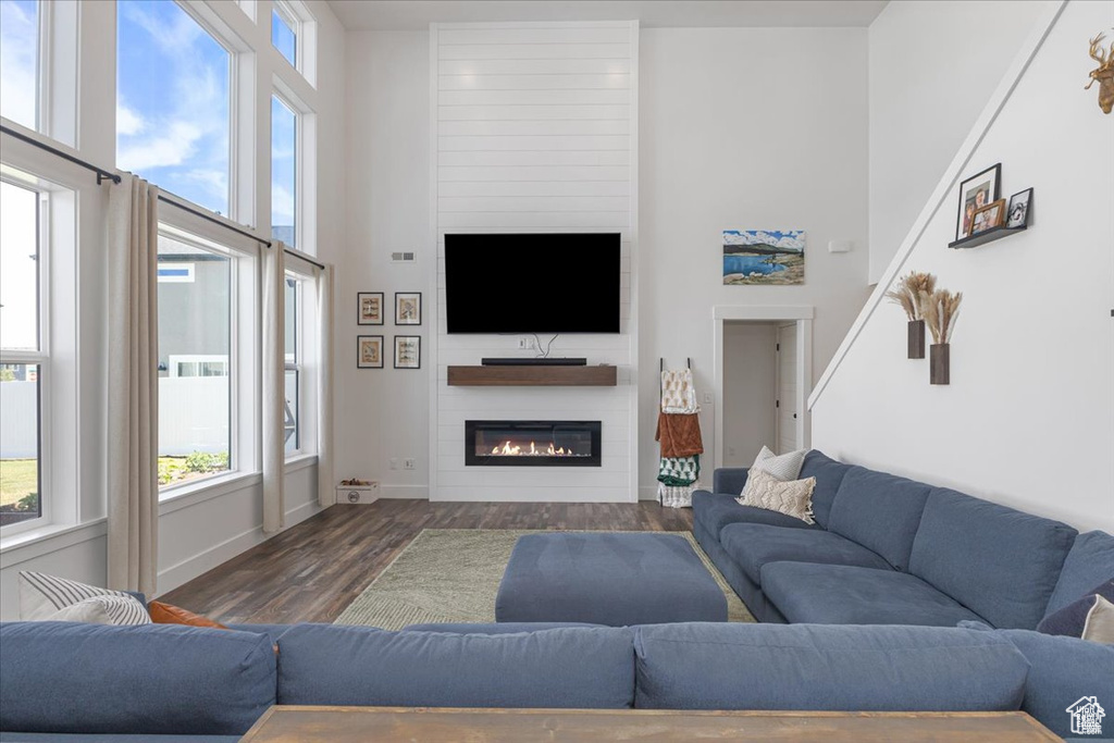 Living room with dark wood-type flooring, plenty of natural light, a large fireplace, baseboards, and a towering ceiling
