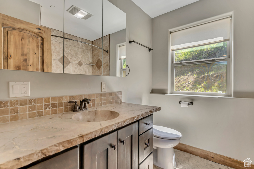 Bathroom with tiled shower, vanity, tasteful backsplash, toilet, and baseboards