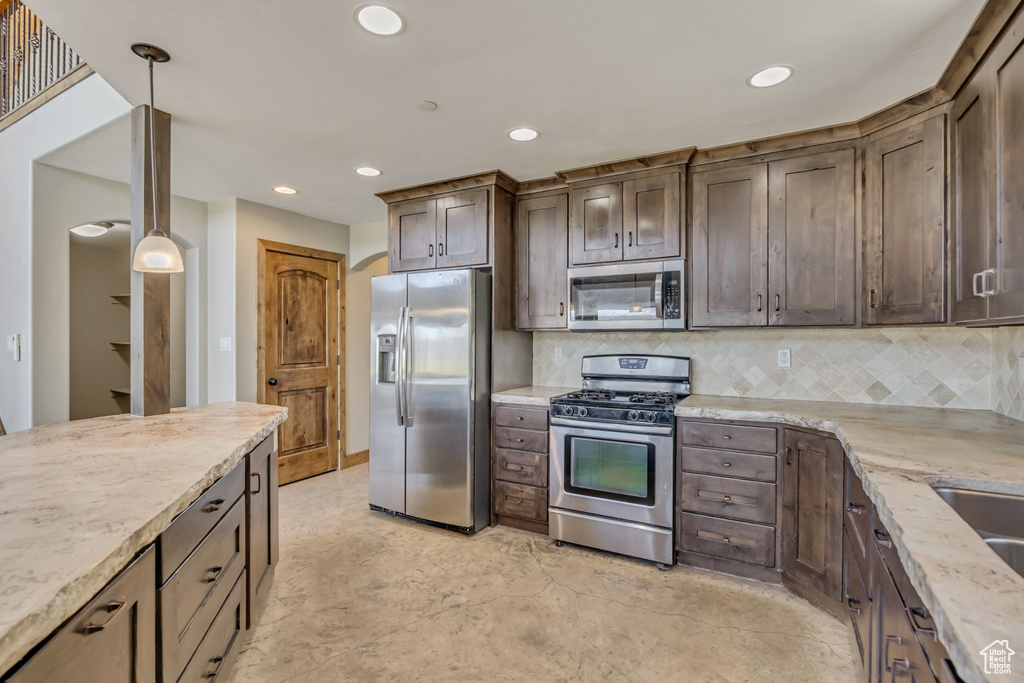 Kitchen featuring stainless steel appliances, dark brown cabinets, recessed lighting, backsplash, and light stone countertops