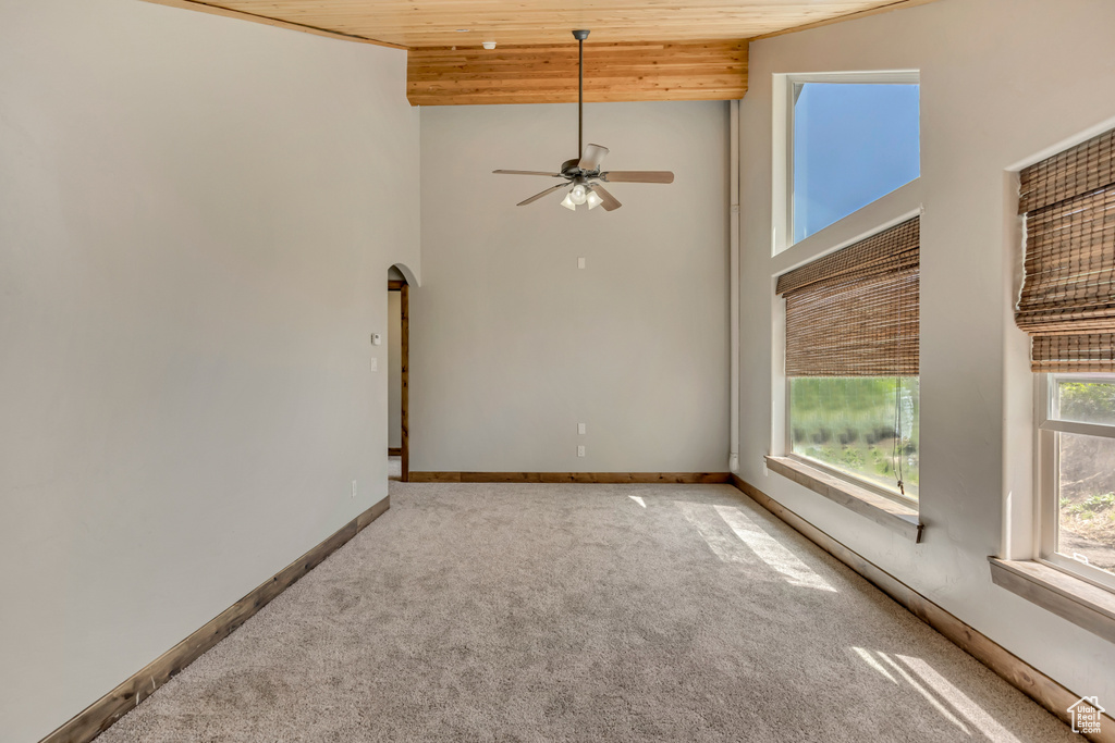 Spare room with wood ceiling, arched walkways, carpet floors, a towering ceiling, and ceiling fan