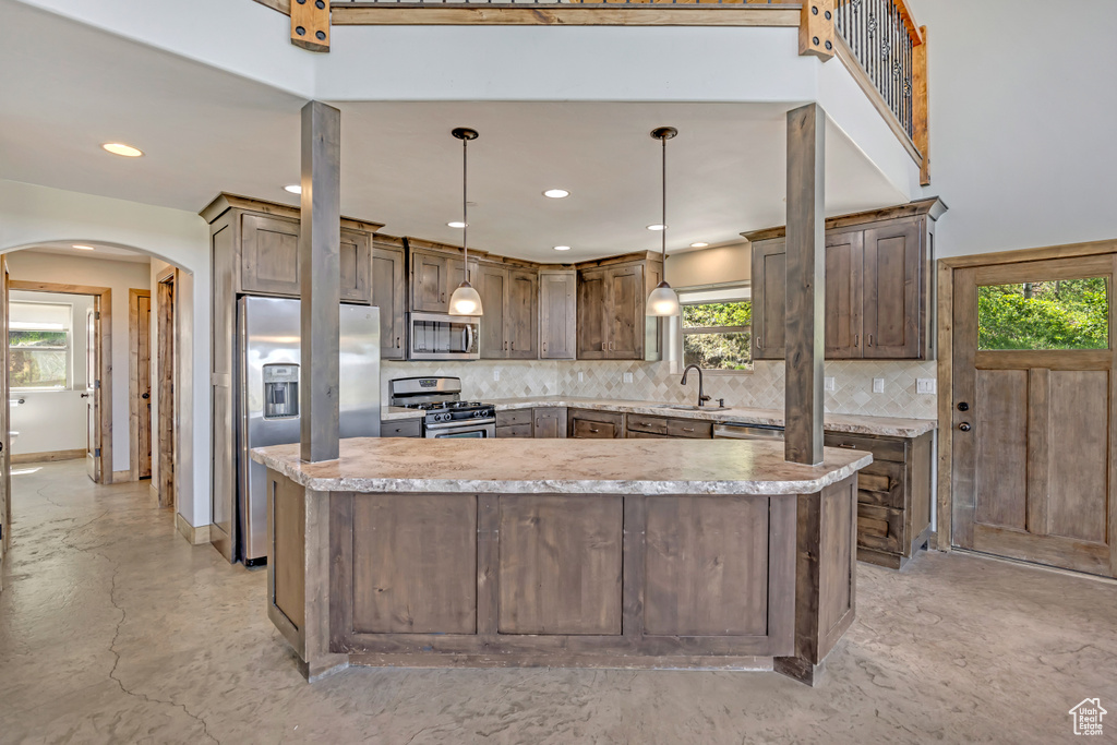 Kitchen featuring stainless steel appliances, arched walkways, a sink, tasteful backsplash, and a center island