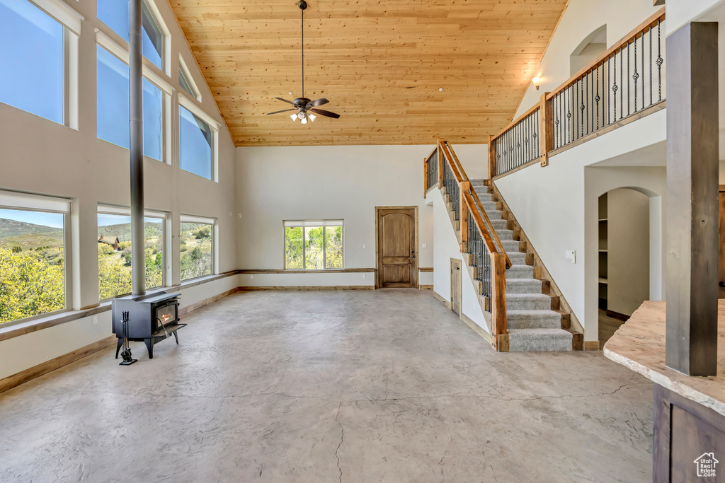 Unfurnished living room with high vaulted ceiling, wood ceiling, a ceiling fan, a wood stove, and concrete floors