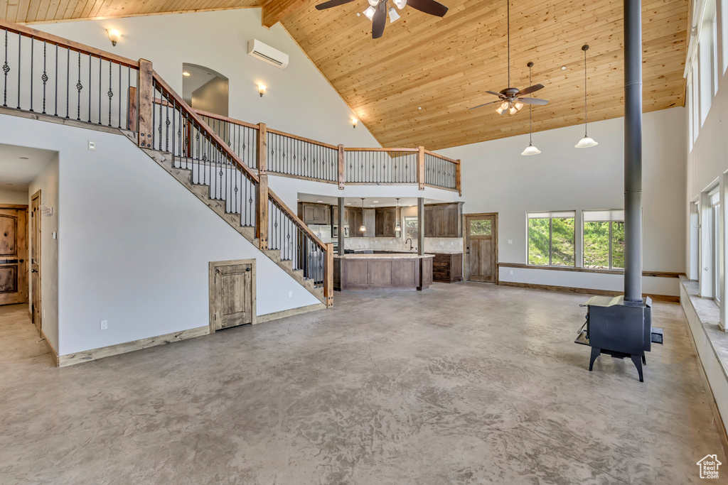 Unfurnished living room featuring a wood stove, high vaulted ceiling, ceiling fan, concrete flooring, and stairs