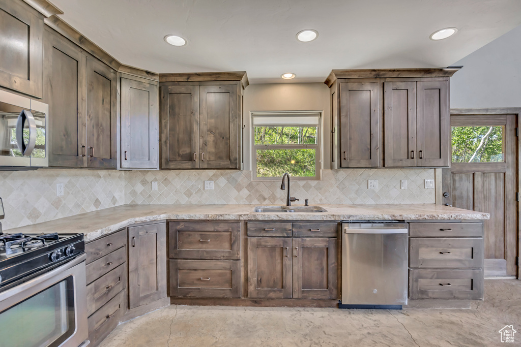 Kitchen with appliances with stainless steel finishes, a sink, backsplash, recessed lighting, and light stone countertops