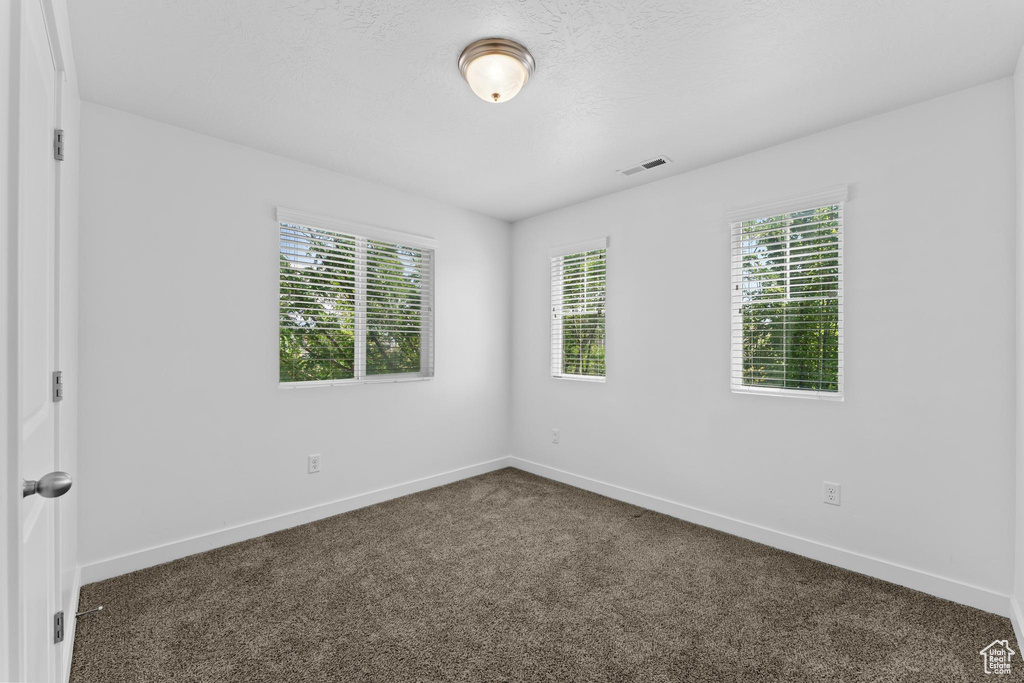 Unfurnished room with baseboards, plenty of natural light, and dark carpet