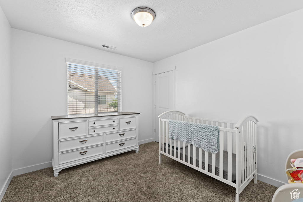 Bedroom with dark colored carpet, baseboards, a textured ceiling, and a nursery area