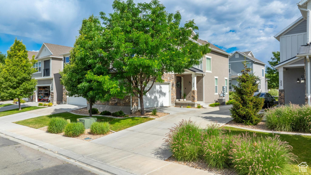 View of property hidden behind natural elements featuring driveway, a residential view, stone siding, and stucco siding
