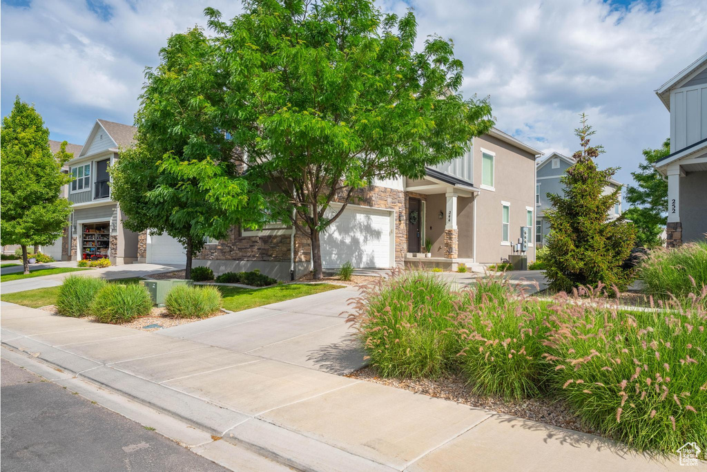 View of property hidden behind natural elements featuring stone siding, driveway, and a garage