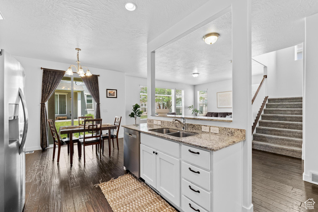 Kitchen with appliances with stainless steel finishes, a sink, a textured ceiling, dark wood-style floors, and a chandelier