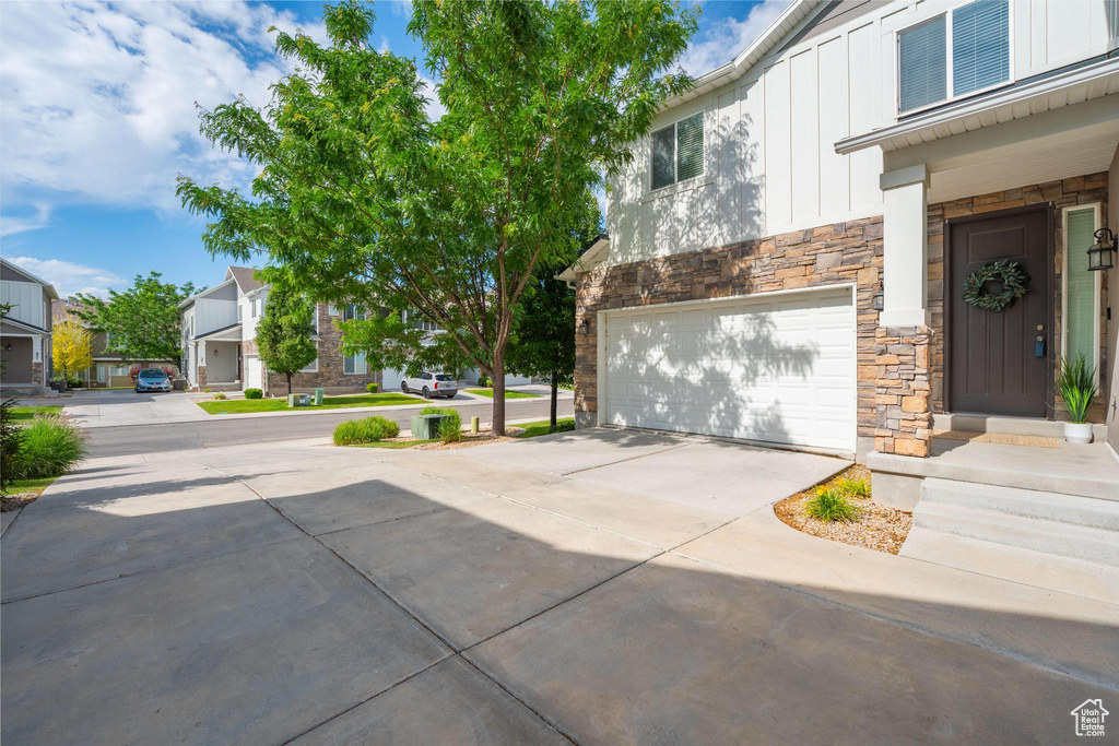 Exterior space featuring stone siding, board and batten siding, a garage, driveway, and a residential view