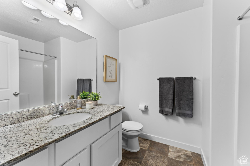 Bathroom featuring baseboards, stone finish floors, vanity, toilet, and a shower
