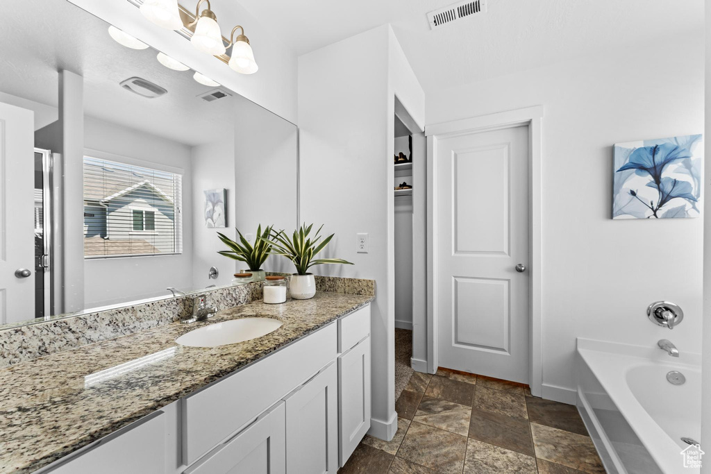 Full bathroom with baseboards, stone finish flooring, vanity, a garden tub, and a closet