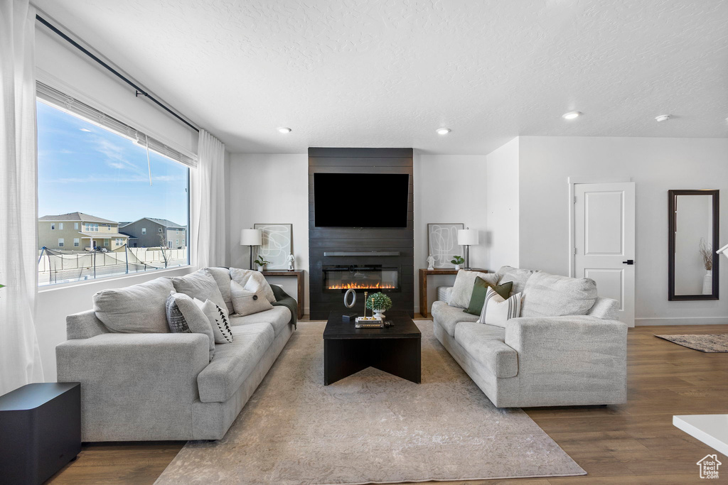Living area featuring wood finished floors, a textured ceiling, a large fireplace, recessed lighting, and baseboards