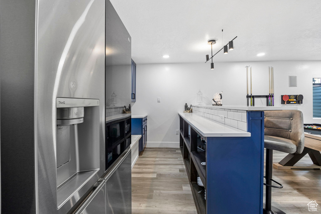 Kitchen with blue cabinetry, stainless steel fridge with ice dispenser, a kitchen breakfast bar, a peninsula, and light countertops