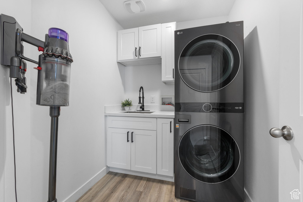 Laundry area featuring stacked washer / drying machine, cabinet space, light wood-type flooring, and baseboards