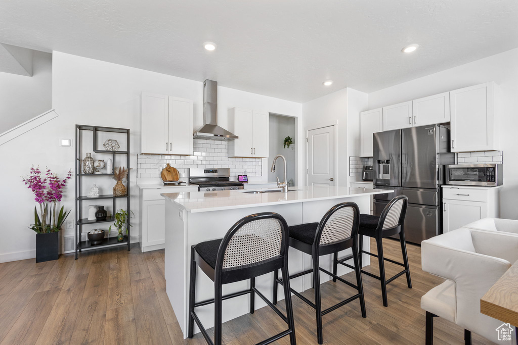 Kitchen featuring stainless steel appliances, wall chimney range hood, a sink, tasteful backsplash, and recessed lighting
