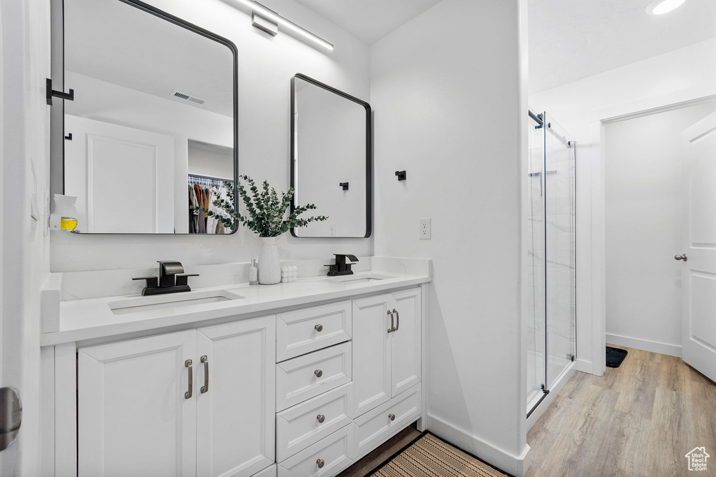Full bath featuring a stall shower, double vanity, wood finished floors, and baseboards