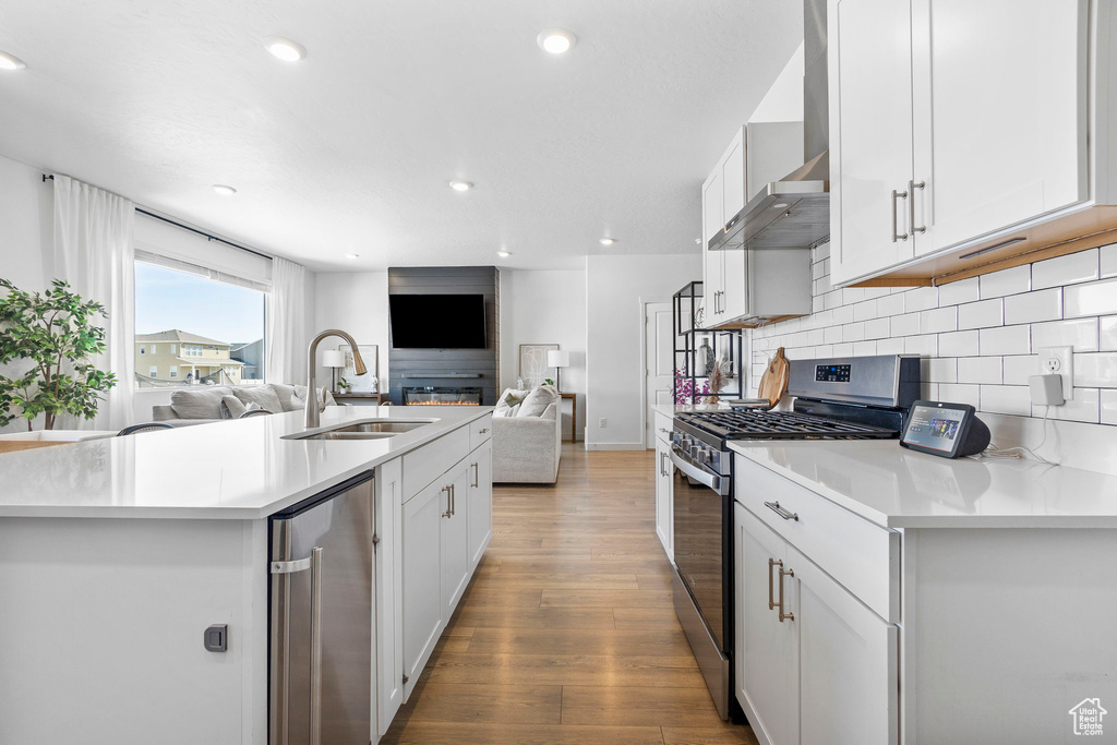 Kitchen with stainless steel gas range, a sink, wall chimney range hood, open floor plan, and wood finished floors