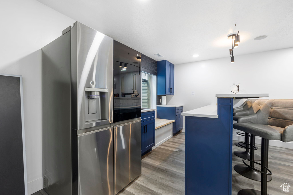 Kitchen with blue cabinets, stainless steel refrigerator with ice dispenser, a breakfast bar, light wood-style floors, and light countertops