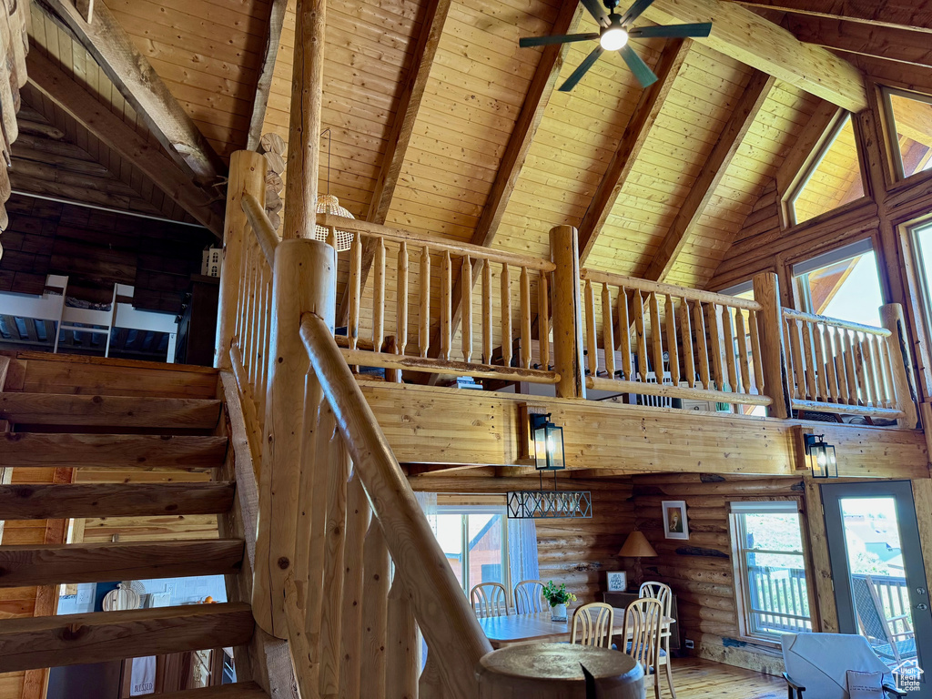 Staircase featuring wood ceiling with exposed beams, high vaulted ceiling, ceiling fan, rustic walls, and wood finished floors