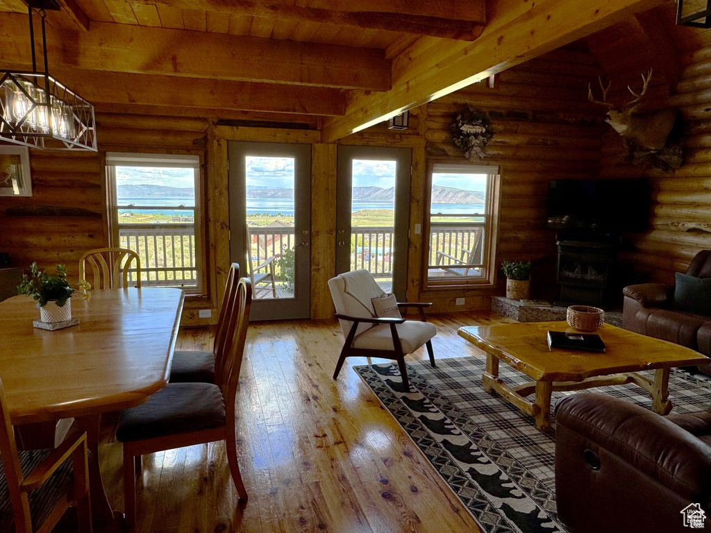 Living area with rustic walls, wood ceiling with exposed beams, light wood-type flooring, and a fireplace with raised hearth